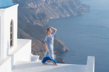 Santorini, Yunanistan onun tatil zevk beyaz ve mavi elbiseli mutlu kadın. Caldera ve Ege Denizi üzerinden Imerovigli görüntüleyin.