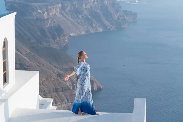 Lycklig kvinna i vita och blå klänning som njuter av sin semester på Santorini, Grekland. Visa på Caldera och Egeiska havet från Imerovigli. — Stockfoto