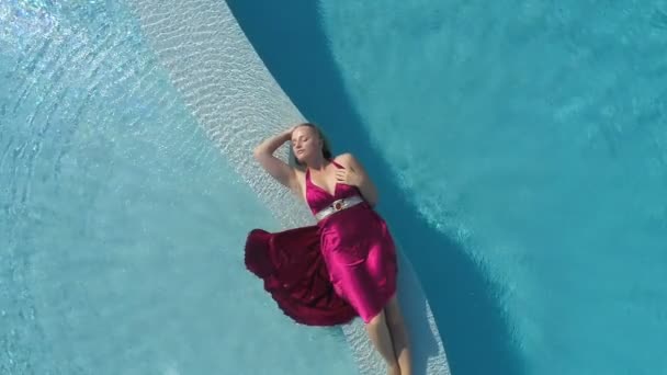 Giovane donna bionda in abito rosso sdraiata in piscina — Video Stock