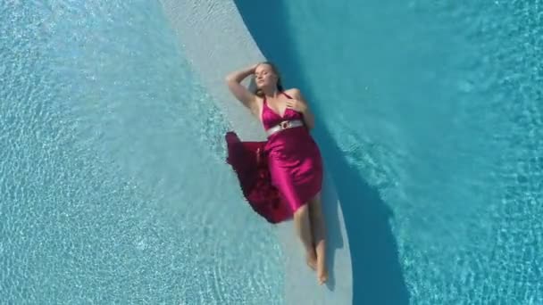 Mujer rubia joven en vestido rojo tumbado en la piscina — Vídeo de stock