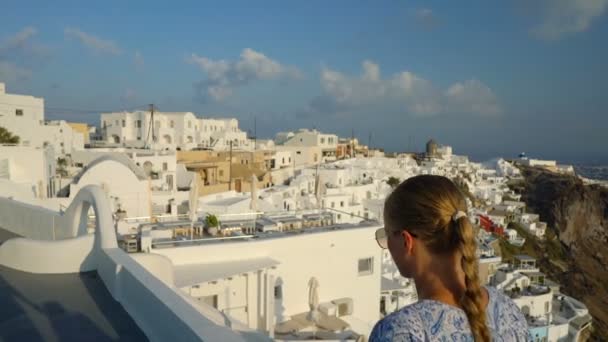 Ευτυχισμένη γυναίκα στο λευκό και το μπλε φόρεμα που απολαμβάνει τις διακοπές της στη Σαντορίνη, Ελλάδα. Θέα στην Καλντέρα και το Αιγαίο Πέλαγος από το Ημεροβίγλι. Ενεργός, ταξίδια, τουριστικά έννοιες — Αρχείο Βίντεο