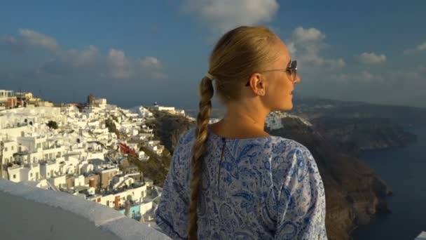 Mulher feliz em vestido branco e azul desfrutando de suas férias em Santorini, Grécia. Vista sobre Caldera e mar Egeu de Imerovigli. Ativo, viagens, conceitos turísticos — Vídeo de Stock