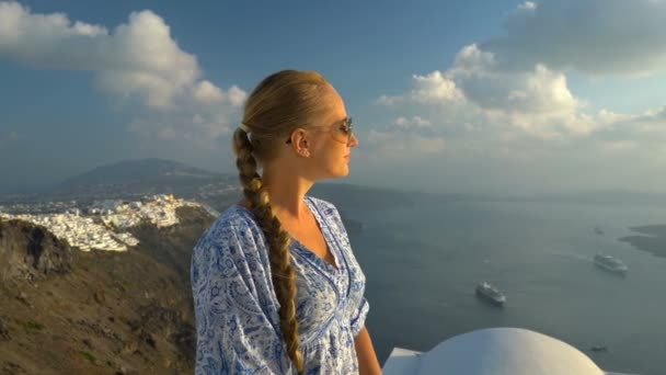 Счастливая женщина в белом и синем платье наслаждается отдыхом на Санторини, Греция. Вид на Кальдеру и Эгейское море из Имеровигли. Активные, путешествия, туристические концепции — стоковое видео