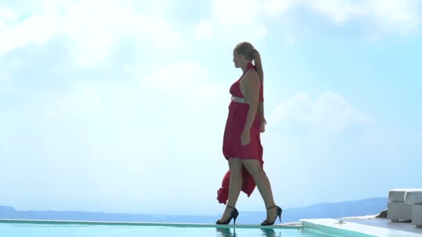 Молодая женщина, идущая вдоль края бассейна наслаждаясь великолепным видом на Санторини — стоковое видео
