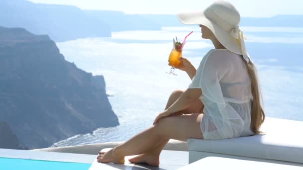 Ung kvinna dricka en cocktail som du njuter av magnifik utsikt över Santorini nära poolen — Stockvideo