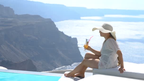 Ung kvinna dricka en cocktail som du njuter av magnifik utsikt över Santorini nära poolen — Stockvideo