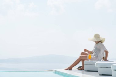 Genç kadın havuz kenarında Santorini büyüleyici bir manzarasına sahip bir kokteyl içme