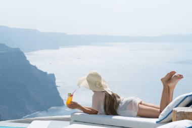 Genç kadın havuz kenarında Santorini büyüleyici bir manzarasına sahip bir kokteyl içme