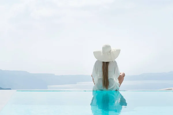 Mladá žena se těší nádherný výhled na Santorini v blízkosti bazénu. — Stock fotografie