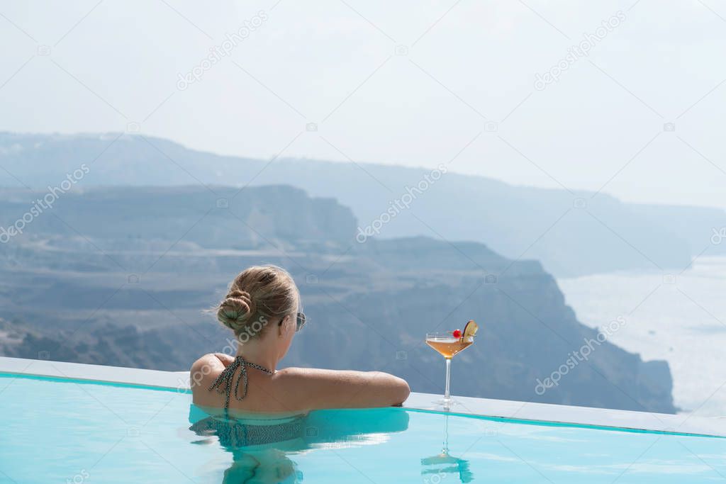 Young woman relaxing in the pool with a gorgeous view on Santorini.