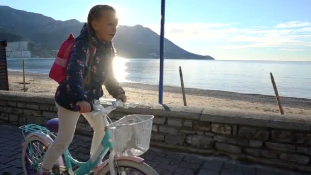 Sex år gammal flicka rider en cykel till skolan på morgonen längs havet — Stockvideo