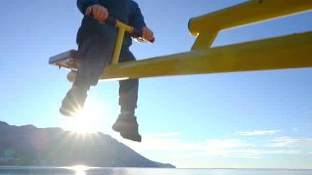 Menino de três anos balançando em um balanço na manhã ensolarada na praia — Vídeo de Stock