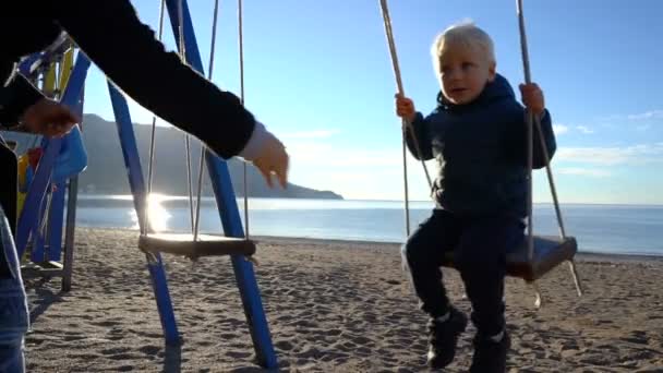 Lengő a napsütéses reggel hinta a strandon három éves fiú — Stock videók