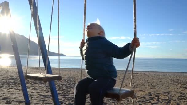 Τρίχρονο αγόρι κουνιέστε σε μία κούνια το ηλιόλουστο πρωί στην παραλία — Αρχείο Βίντεο