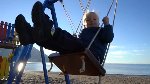 在海岸阳光明媚的早晨, 一名3岁的男孩和一名6岁的女孩在秋千上荡秋千 — 图库视频影像