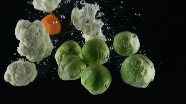 Mezcla de verduras cae en el agua sobre un fondo negro — Vídeos de Stock