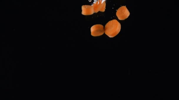 Chopped carrot falls in water on black background — Stock Video