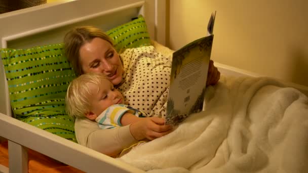 माँ और बच्चे बेटा बिस्तर में एक किताब पढ़ रहे हैं — स्टॉक वीडियो