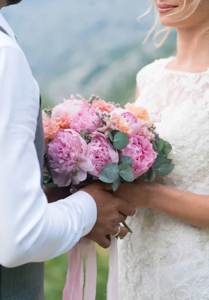 Paar houden een bruiloft boeket van roze pioenrozen — Stockfoto