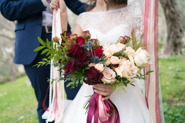 Bouquet de mariage rouge-rose de roses et de verdure entre les mains de la mariée — Photo