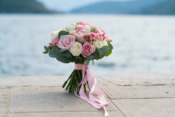 Bouquet da sposa rosa-bianco sorge su un molo vicino al mare Immagine Stock