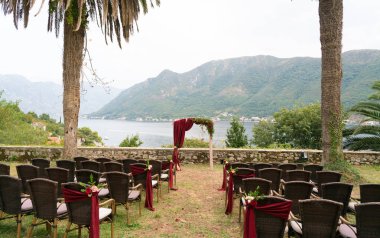 Kemer ve koyu kırmızı tonlarda düğün töreni için taze çiçeklerle süslü sandalyeler