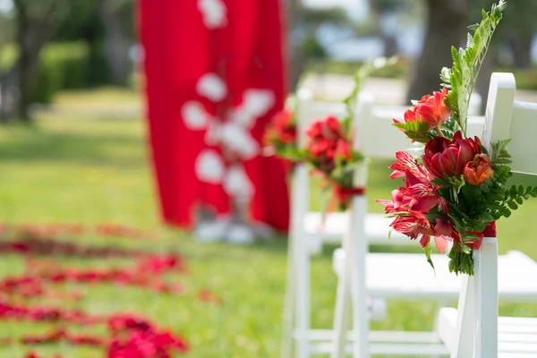 Sillas decoradas con flores frescas en tonos rojos para la ceremonia de boda en el césped verde — Foto de Stock