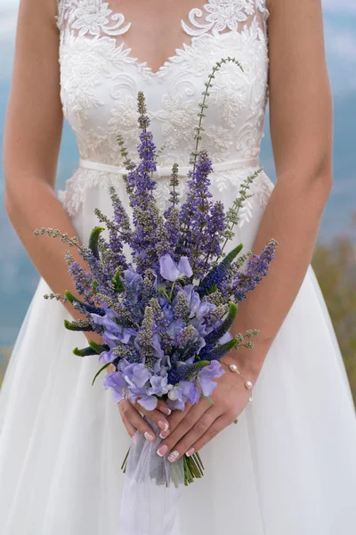 Novia sostiene elegante ramo de flores y hierbas moradas — Foto de Stock