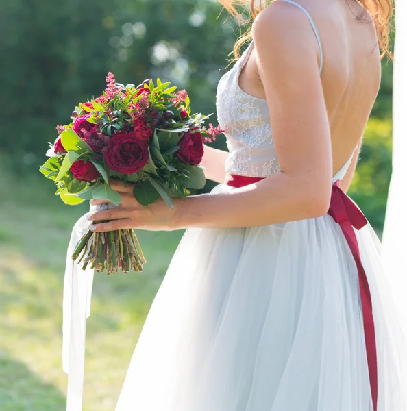 De bruid is het houden van een lichte rode bruiloft-bouquet van verse bloemen en eucalyptus — Stockfoto