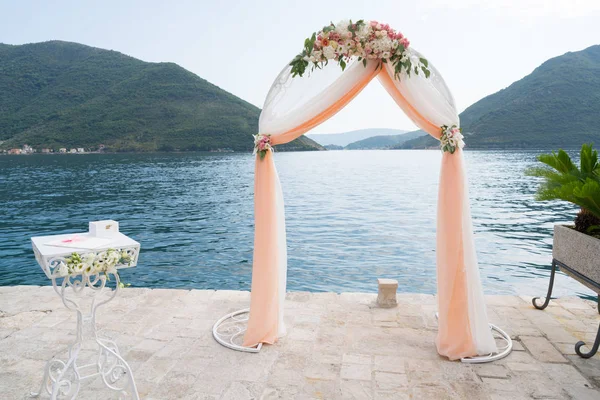 Arco de boda decorado con flores y tela para la ceremonia cerca del mar — Foto de Stock