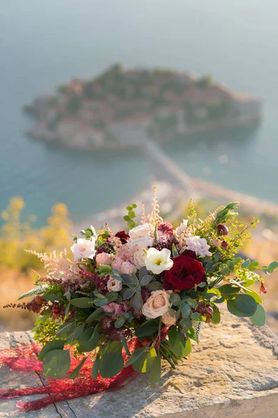 Prachtige bruiloft boeket staat op een steen tegen de achtergrond van het eiland Sveti Stefan — Stockfoto