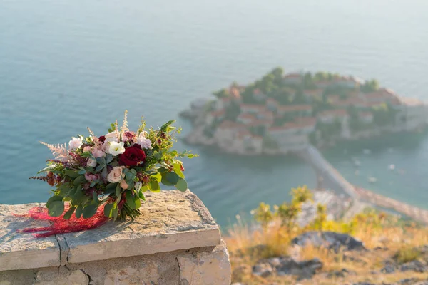 Magnífico buquê de casamento fica em uma pedra contra o fundo da ilha de Sveti Stefan — Fotografia de Stock