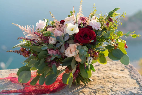 Magnífico buquê de casamento fica em uma pedra nos raios do sol poente — Fotografia de Stock