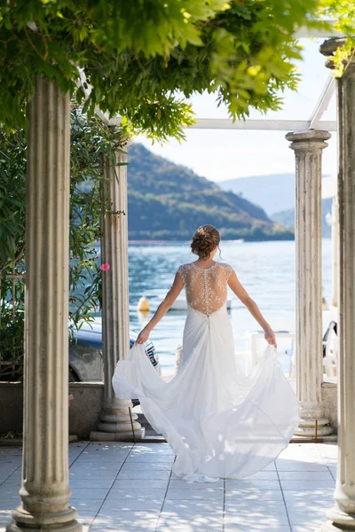 Невеста в свадебном платье ходит по террасе среди колонн на фоне моря — стоковое фото