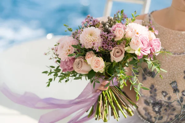 De bruid houdt een boeket roze en Lila bruiloft in haar armen tegen de achtergrond van de zee — Stockfoto