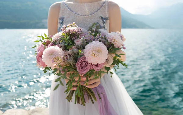 La novia sostiene un ramo de boda rosa y lila en sus brazos contra el fondo del mar — Foto de Stock