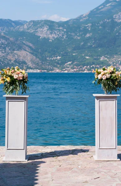 Composizioni floreali sugli stand per una cerimonia nuziale sul molo contro il mare — Foto Stock