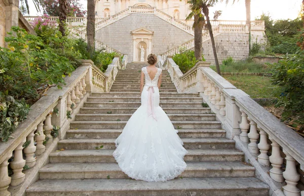 Sposa graziosa sale le scale di pietra in un abito da sposa — Foto Stock