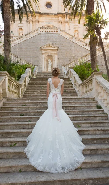 Sposa graziosa sale le scale di pietra in un abito da sposa — Foto Stock