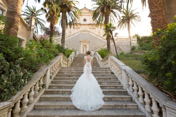 Sposa graziosa sale le scale di pietra in un abito da sposa — Foto Stock