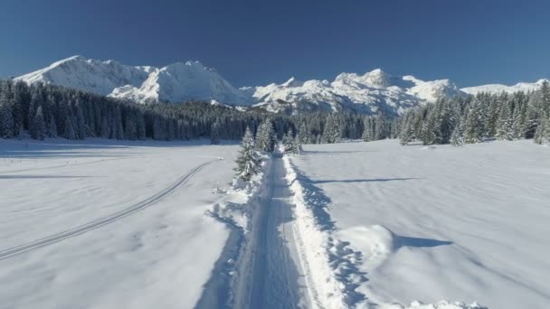 Vlucht over een besneeuwde landweg op een zonnige dag met uitzicht op de bergen — Stockvideo