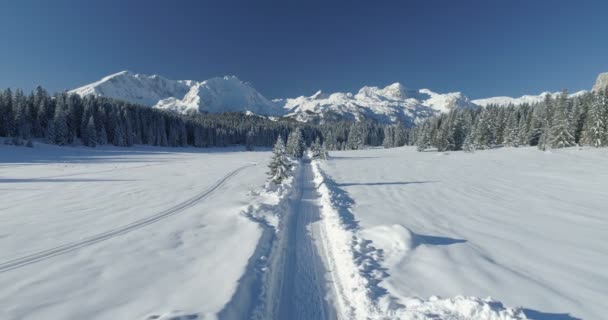 Vuelo sobre una carretera nevada en un día soleado con vistas a las montañas — Vídeos de Stock
