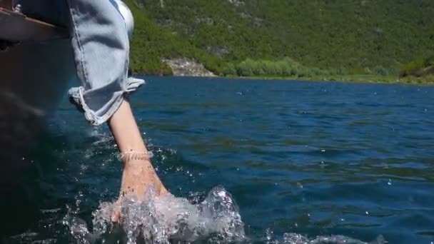 En ung kvinna sitter i en motor båt och sänkte sin hand i vattnet medan han flyttade båten — Stockvideo
