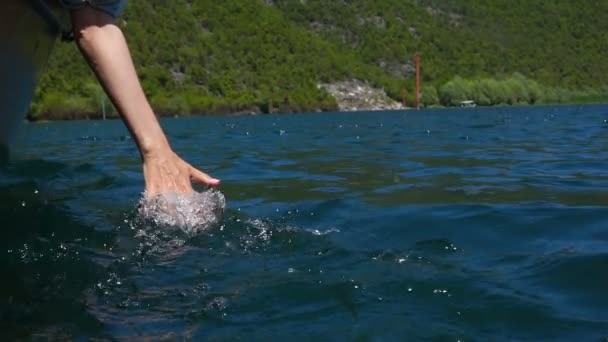 En ung kvinna sitter i en motor båt och sänkte sin hand i vattnet medan han flyttade båten — Stockvideo