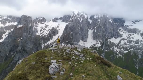 Un excursionista se para en la cima de una montaña y mira las montañas cubiertas de nieve — Vídeos de Stock