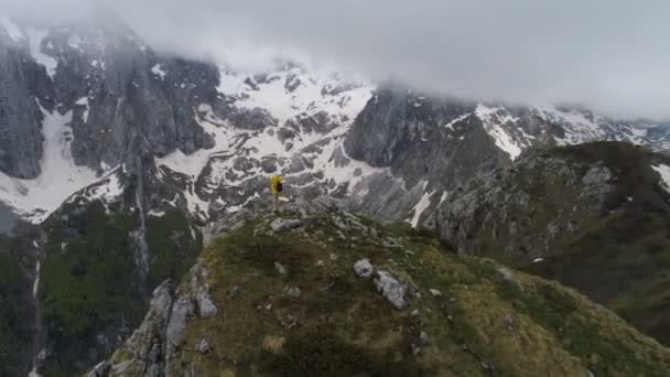 Un excursionista se para en la cima de una montaña y mira las montañas cubiertas de nieve, levantando sus manos en gesto de victoria . — Vídeos de Stock