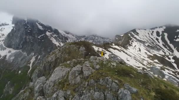 Bir dağın tepesinde duran bir yürüyüşçu, karla kaplı dağlara bakar — Stok video