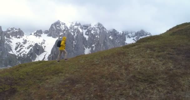 Πεζοπόρος πηγαίνει σε ένα λόφο στο φόντο των χιονισμένα βουνά — Αρχείο Βίντεο