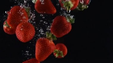 olgun çilek siyah bir arka plan üzerinde suya düşüyor