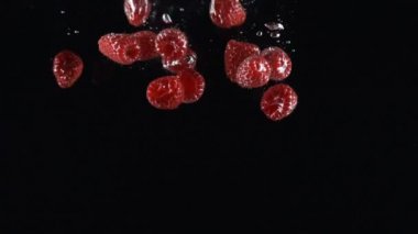 olgun ahududu siyah bir arka plan üzerinde suya düşen